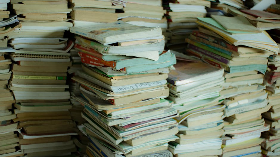A large collection of tightly bound stacks of books and magazines, secured with white plastic strapping, are positioned in an indoor setting, likely a storage or office space. The books vary in size, 